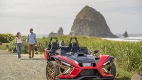The front 3/4 view of a red-black-and-bronze 2022 Polaris Slingshot Signature LE parked by a beach