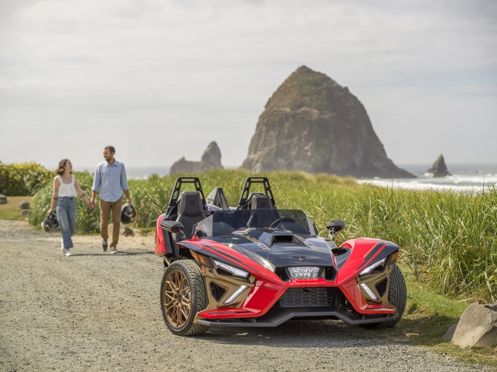 The front 3/4 view of a red-black-and-bronze 2022 Polaris Slingshot Signature LE parked by a beach