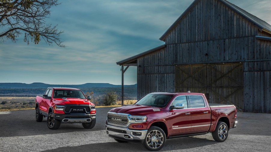 Promo shot of two red Ram 1500 trucks parked in front of an old barn.