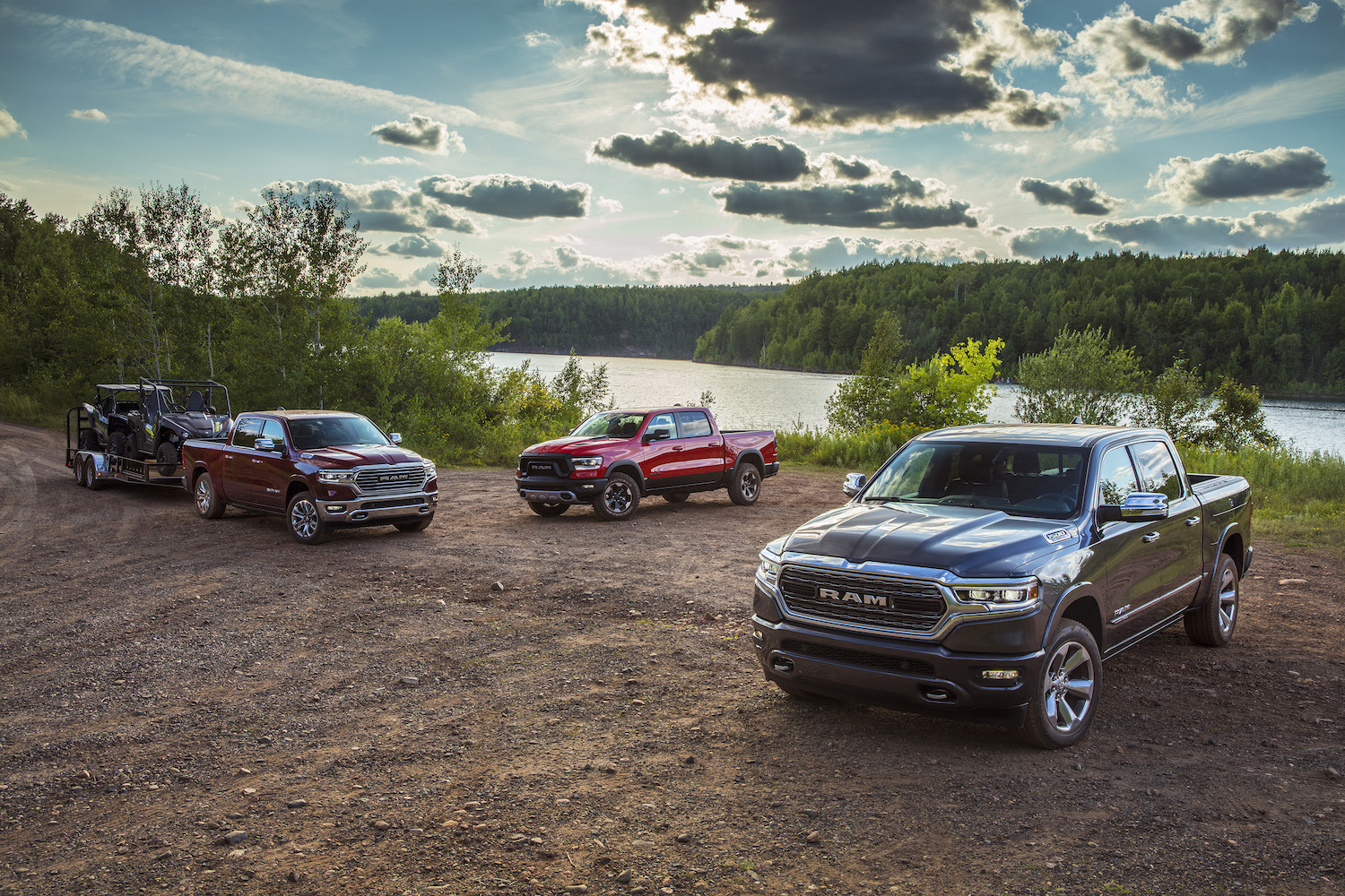 Three 2022 Ram 1500 pickup trucks parked on a dirt road in front of a farm.