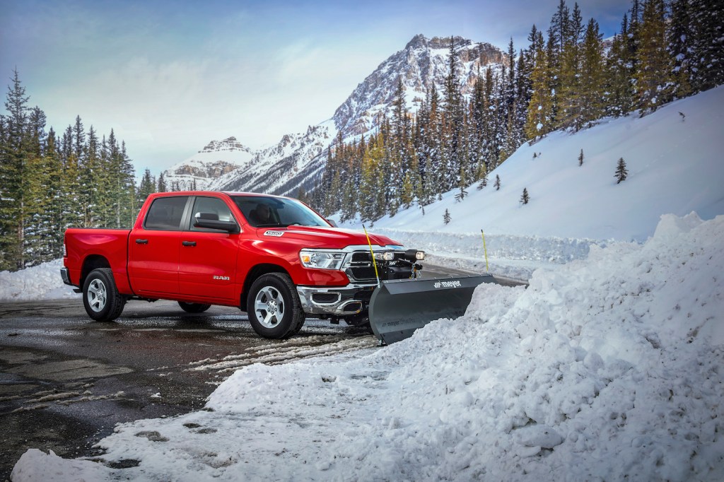 A red 2022 Ram 1500 work truck plowing the snow in a mountain pass.