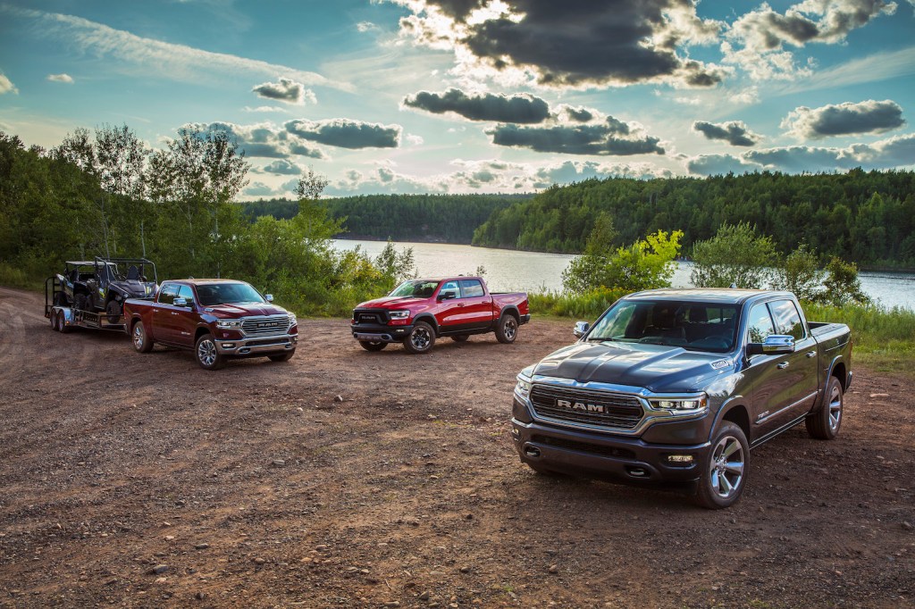 Promo shot of three different 2022 Ram 1500 pickup trucks parked by a rural pond in the summer.