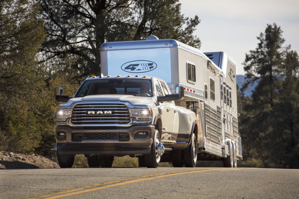 White Ram heavy duty truck towing a large trailer up a tree-lined road.