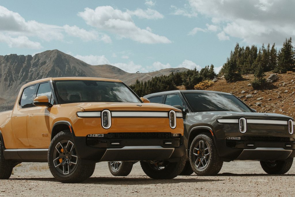 A yellow and a green Rivian electric truck parked in the mountains.