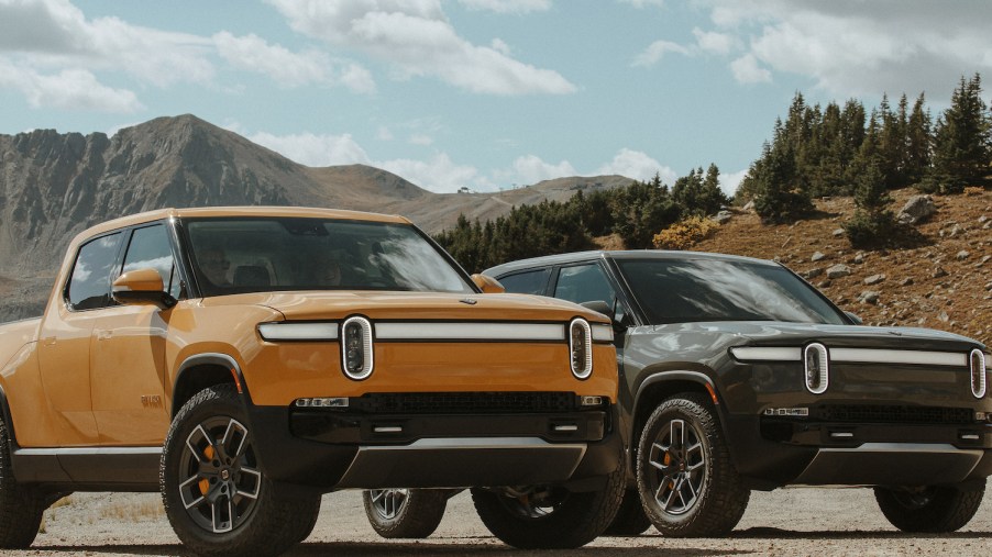 A yellow and a green Rivian electric truck parked in the mountains.