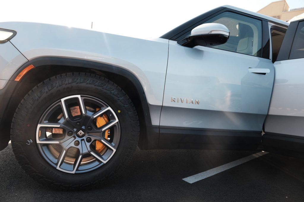The wheel, fender well, and door of a silver Rivian R1T pickup truck EV