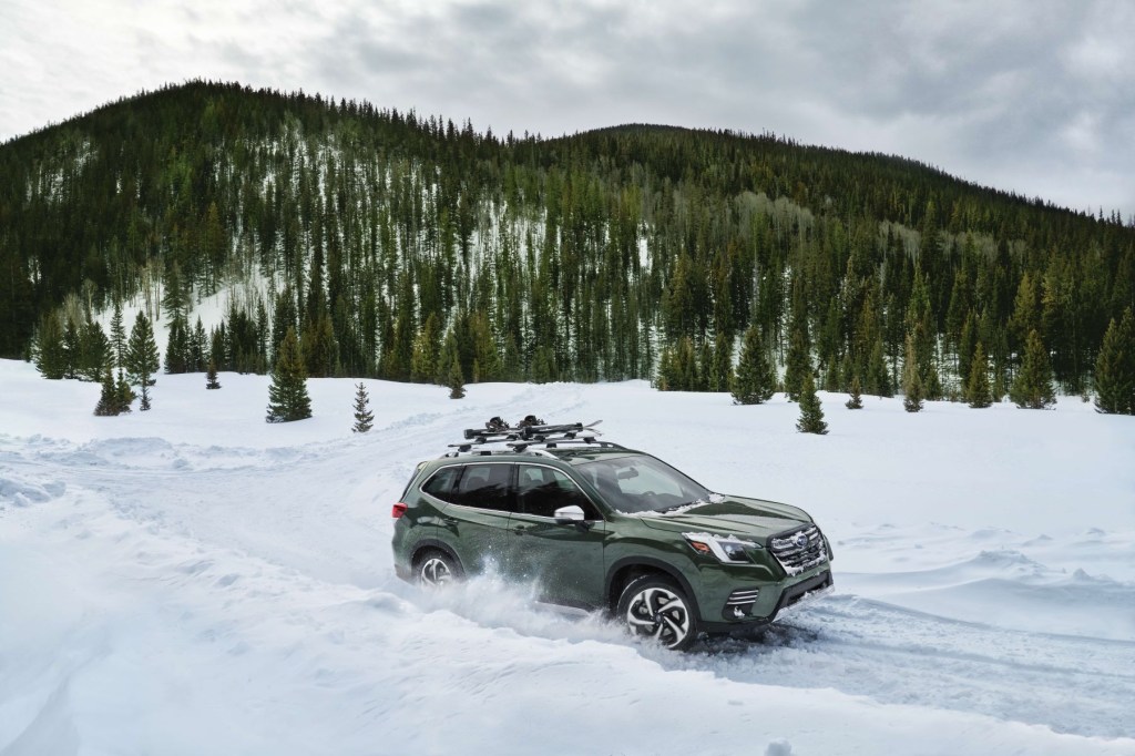 A 2022 Subaru Forester compact crossover SUV with a green paint color driving through snow near a forest