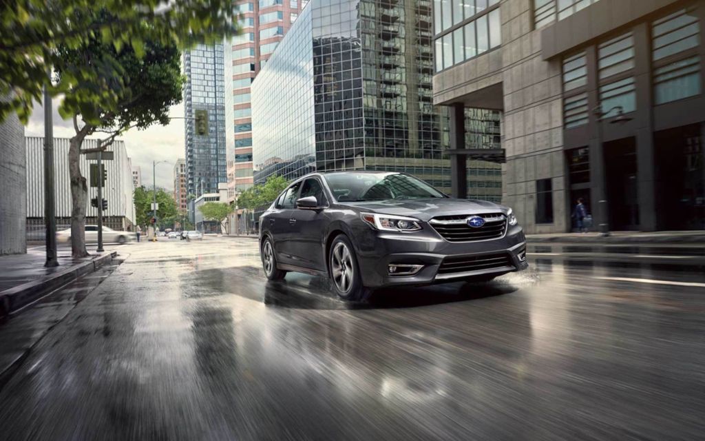 A 2022 Subaru Legacy Limited compact sedan with a Magnetite Gray Metallic paint color option driving through an urban city