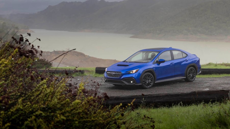 A royal-blue 2022 Subaru WRX parked on wet pavement in front of water and misty mountains