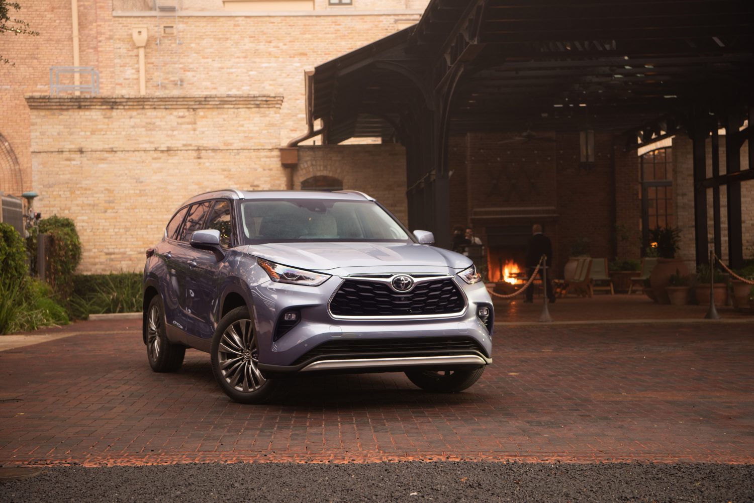 Promo shot of a blue 2022 Toyota Highlander Platinum crossover SUV parked in front of a white brick building.