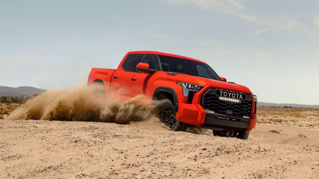 Red Toyota Tundra truck off-roading through a desert, throwing up clouds of dust.