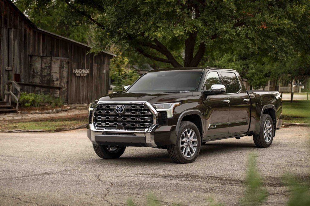 Promo photo of a brown, 2022 Toyota Tundra pickup truck parked in front of an old barn and some trees.