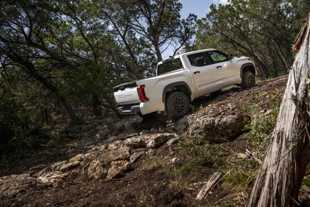 White 4x4 pickup truck climbing up a series of rocks in the woods.