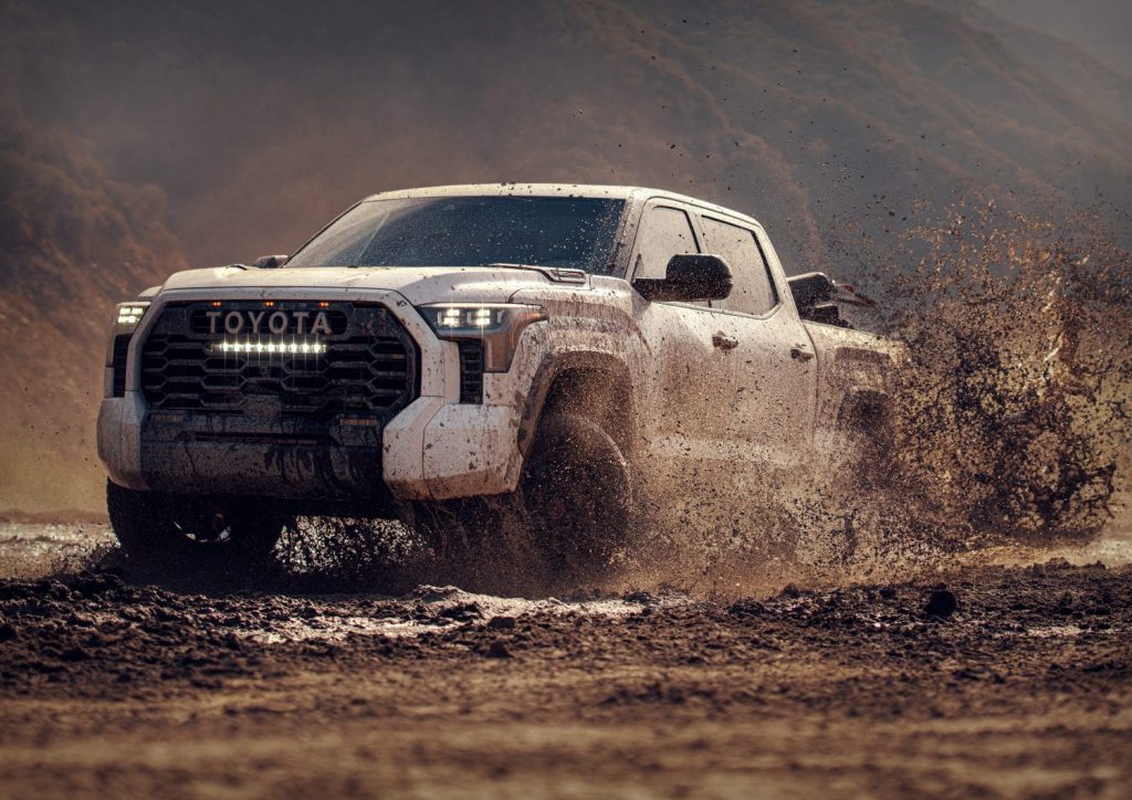 Toyota Tundra showing off its reliability by off-roading through deep mud, a steep gorge in the background.