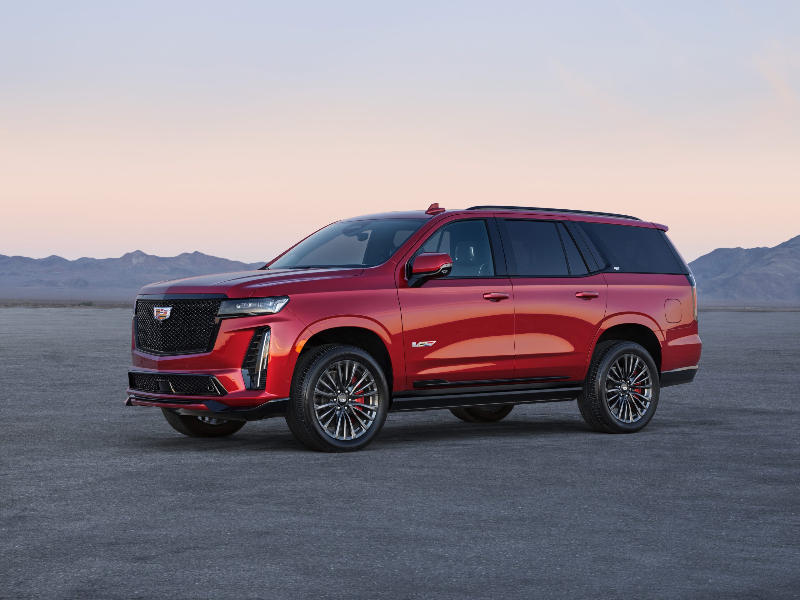 A 3/4 profile view of a red pre-production 2023 Cadillac Escalade V-Series SUV parked with mountains in the background.
