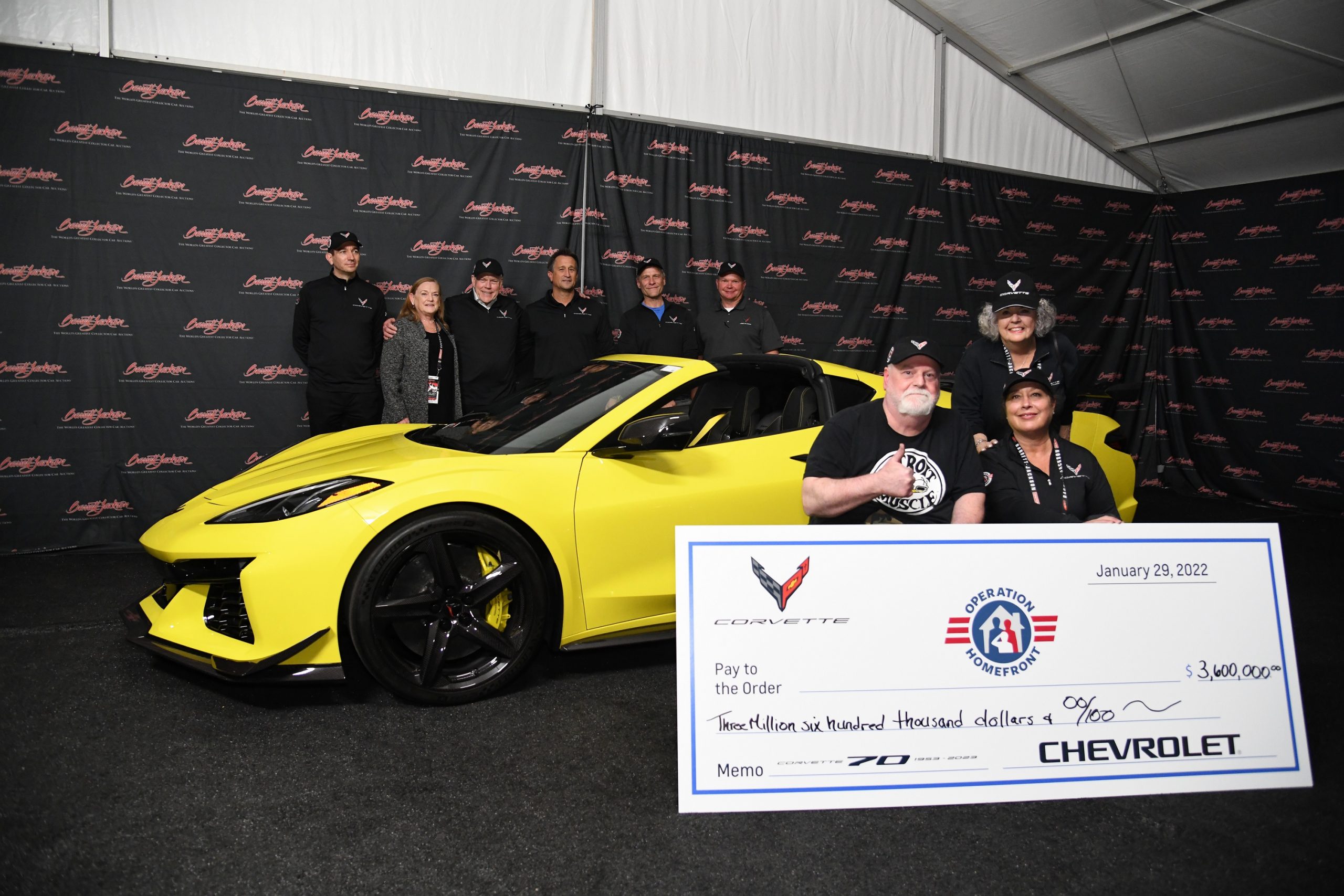 A yellow 2023 Chevrolet Corvette shot with a check made out to charity Operation Homefront