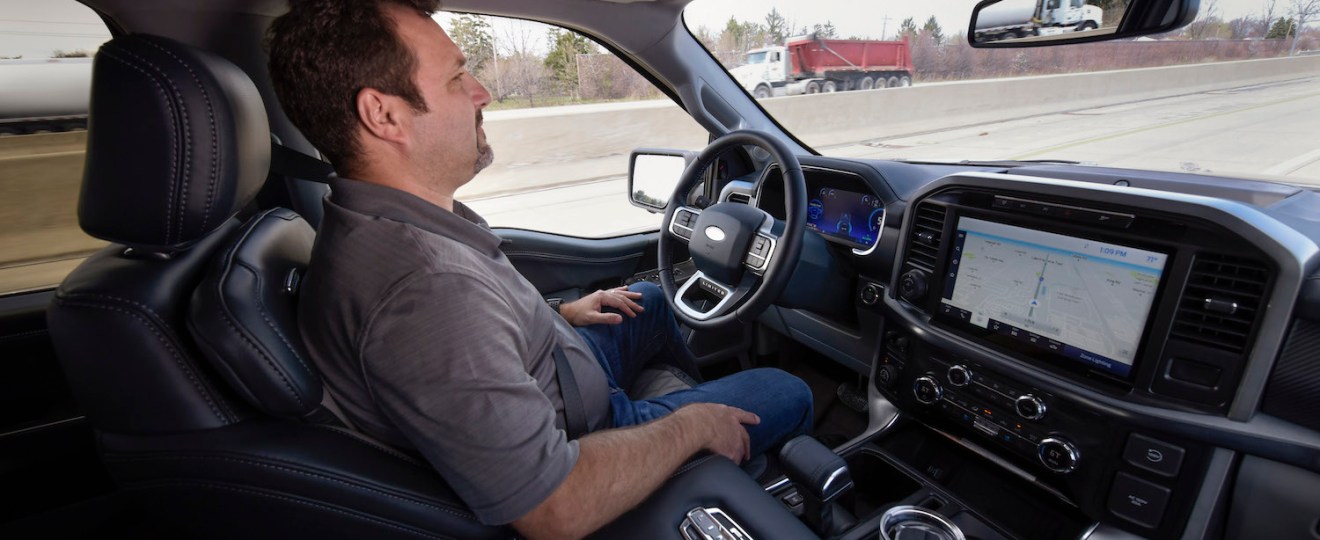 A man demonstrating Ford's BlueCruise software by driving his F 150 pickup truck hands-free.