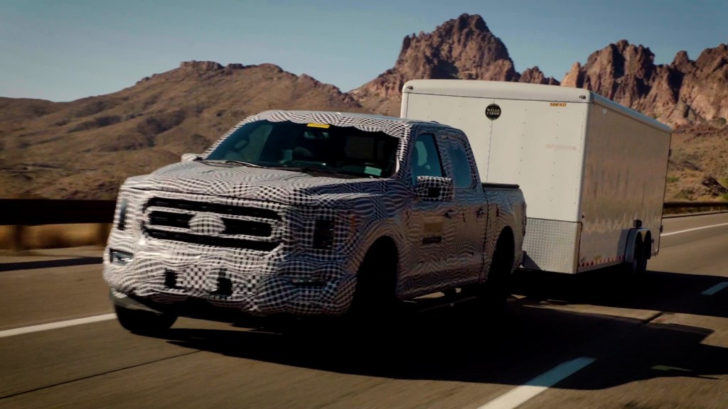 A Ford F 150 work truck with a hybrid PowerBoost engine towing a trailer up a mountain pass in the desert.