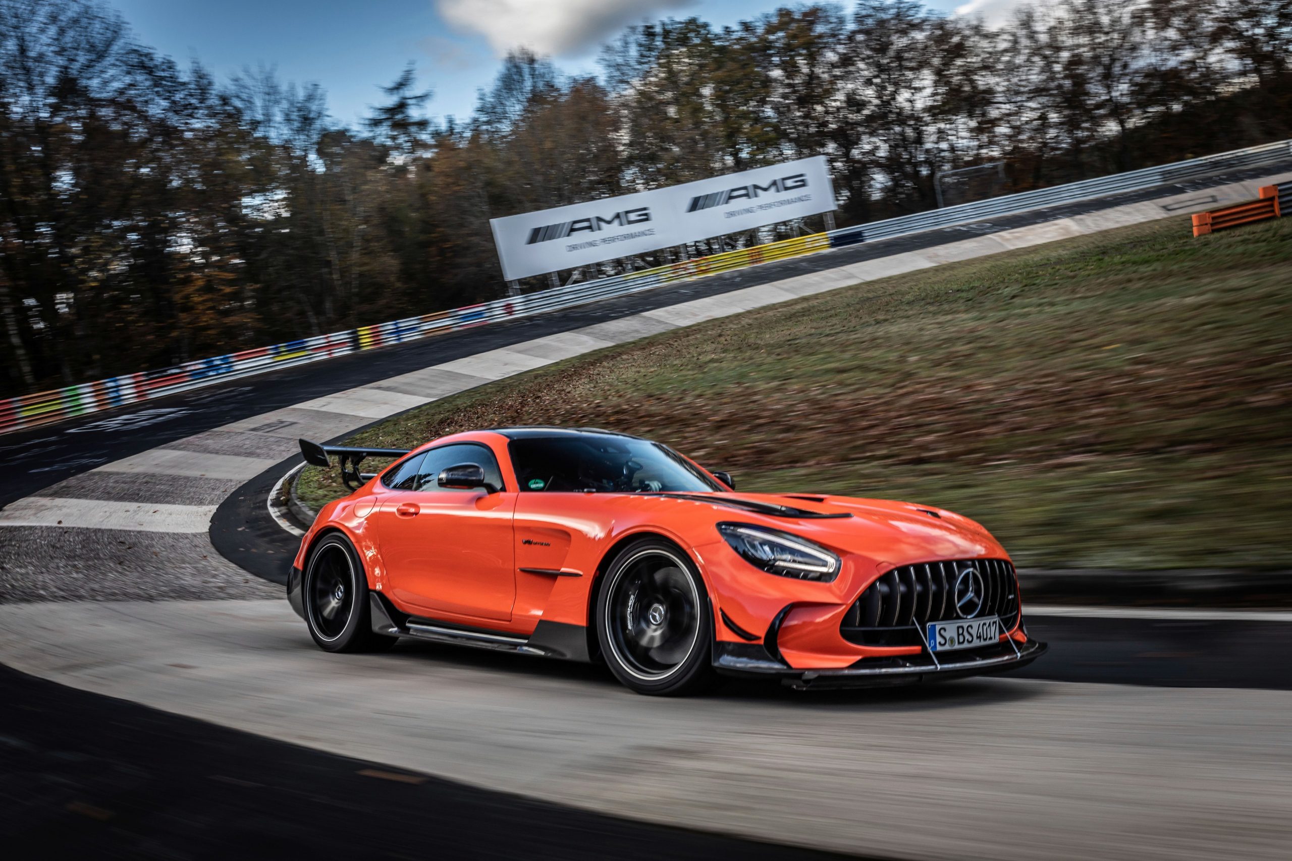 A profile view of an orange and black 2021 Mercedes-AMG GT Black Series car driving around a banked corner at a race track.