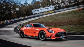 A profile view of an orange and black 2021 Mercedes-AMG GT Black Series car driving around a banked corner at a race track.