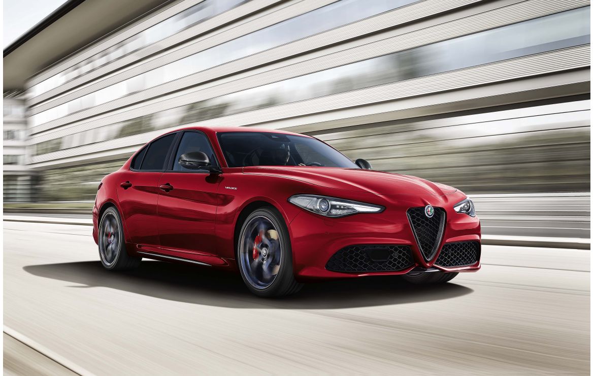 A 3/4 front view of a red 2022 Alfa Romeo Giulia driving on a race track with a blurred background. 
