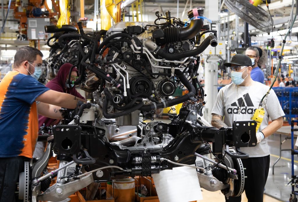 Factory workers installing a Dodge Hellcat engine into a Ram 1500 TRX pickup truck chassis.