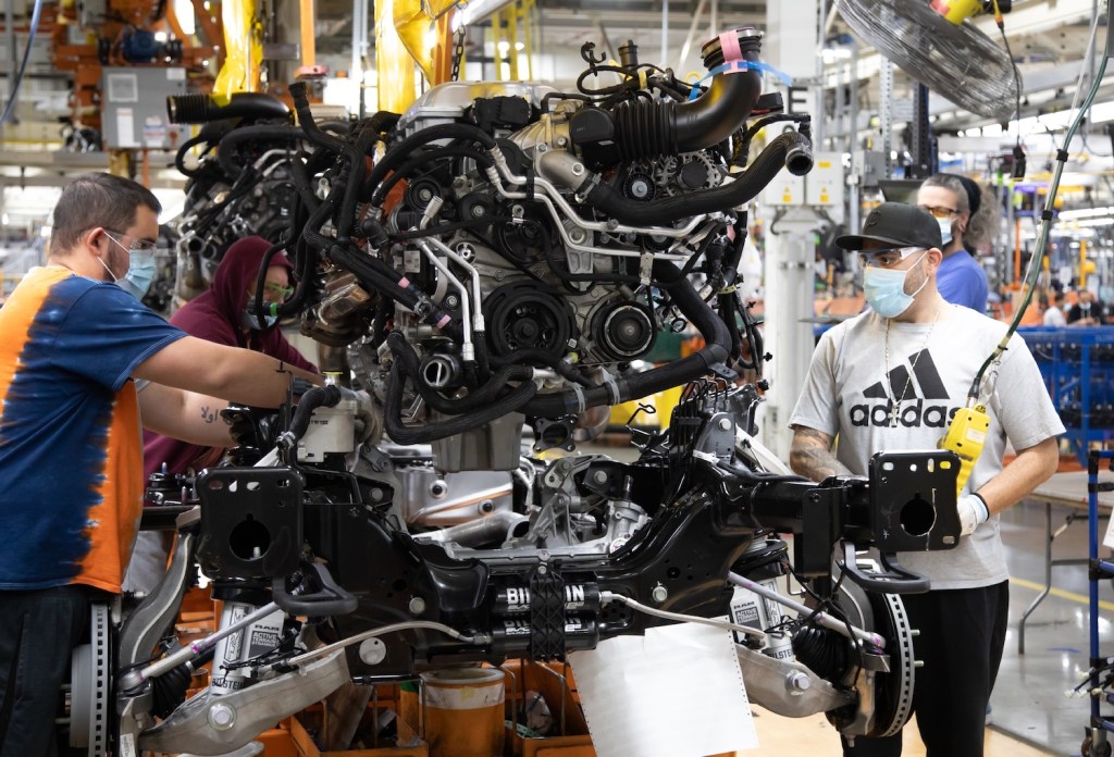 Factory workers installing a Dodge Hellcat engine in a Ram 1500 TRX pickup truck chassis.