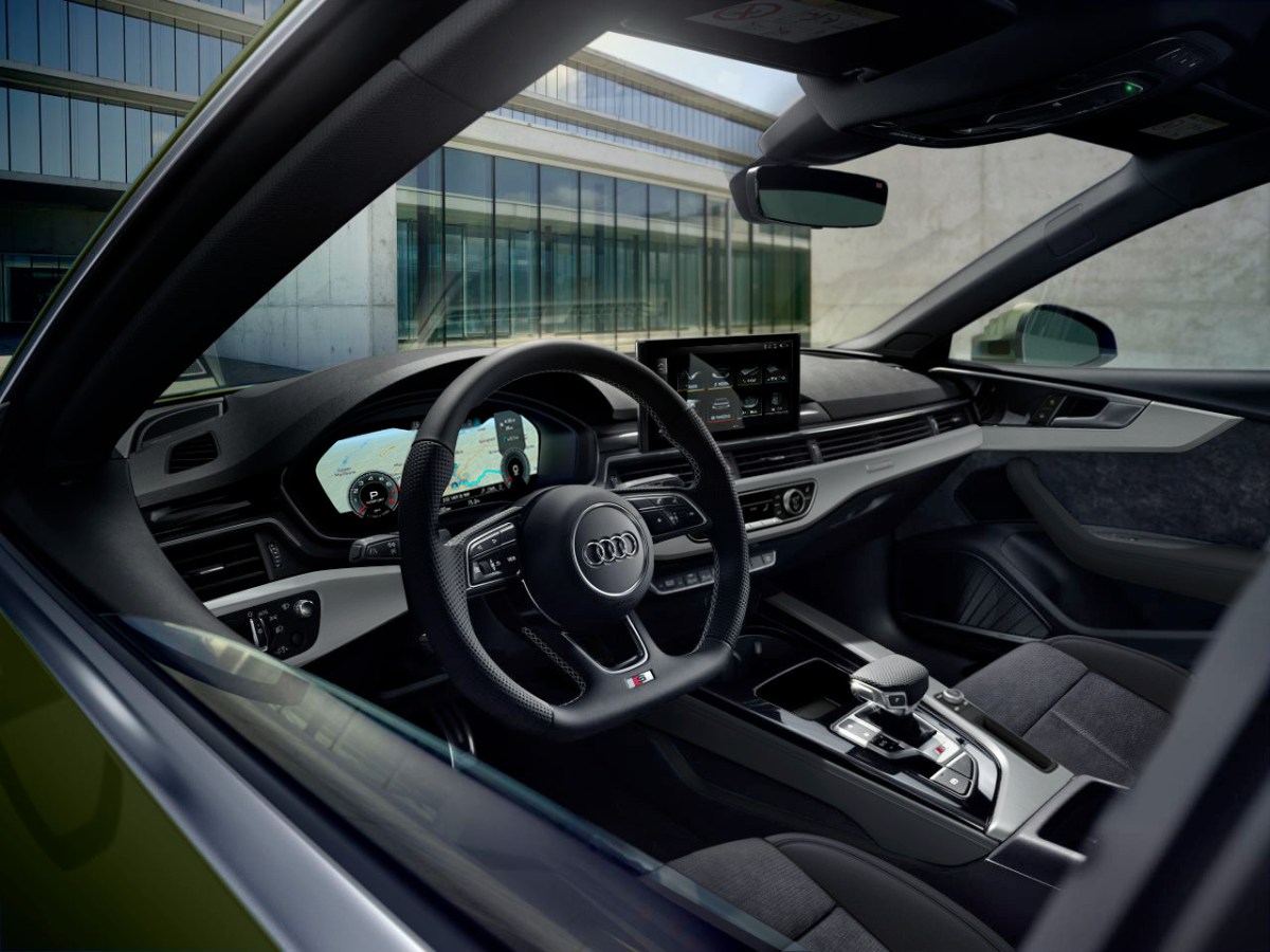 An interior view, as seen through the driver's window, of a 2020 Audi A5 Coupe. Images shows steering wheel, dashboard and infotainment system.