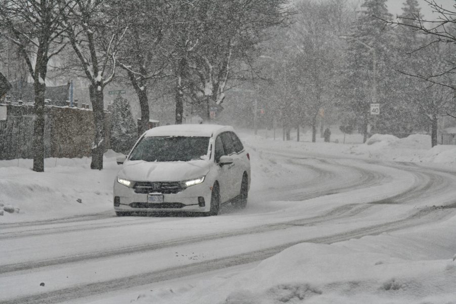 A white car driving down the road during a winter storm.