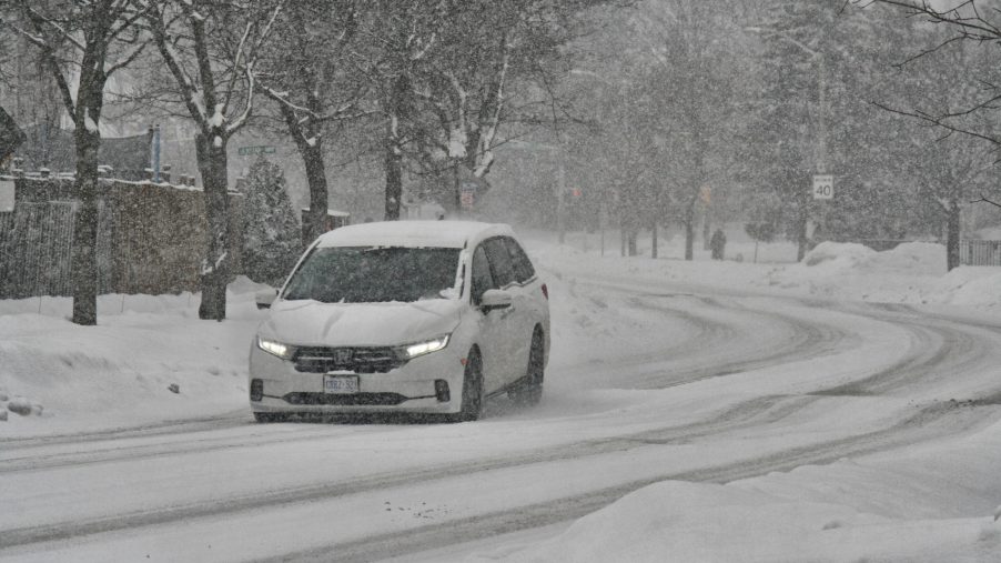 A white car driving down the road during a winter storm.