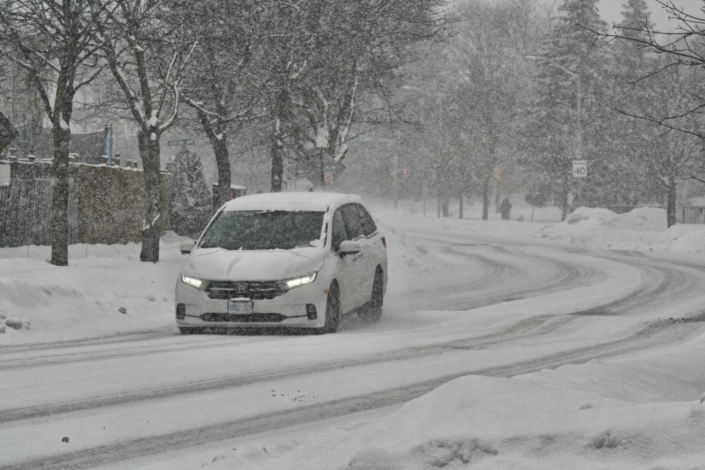 A white car driving down the road during a winter storm. 