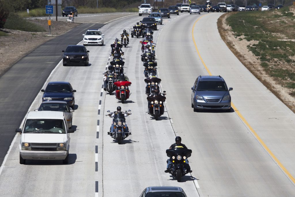 A line of motorcycle riders on the highway surrounded by cars