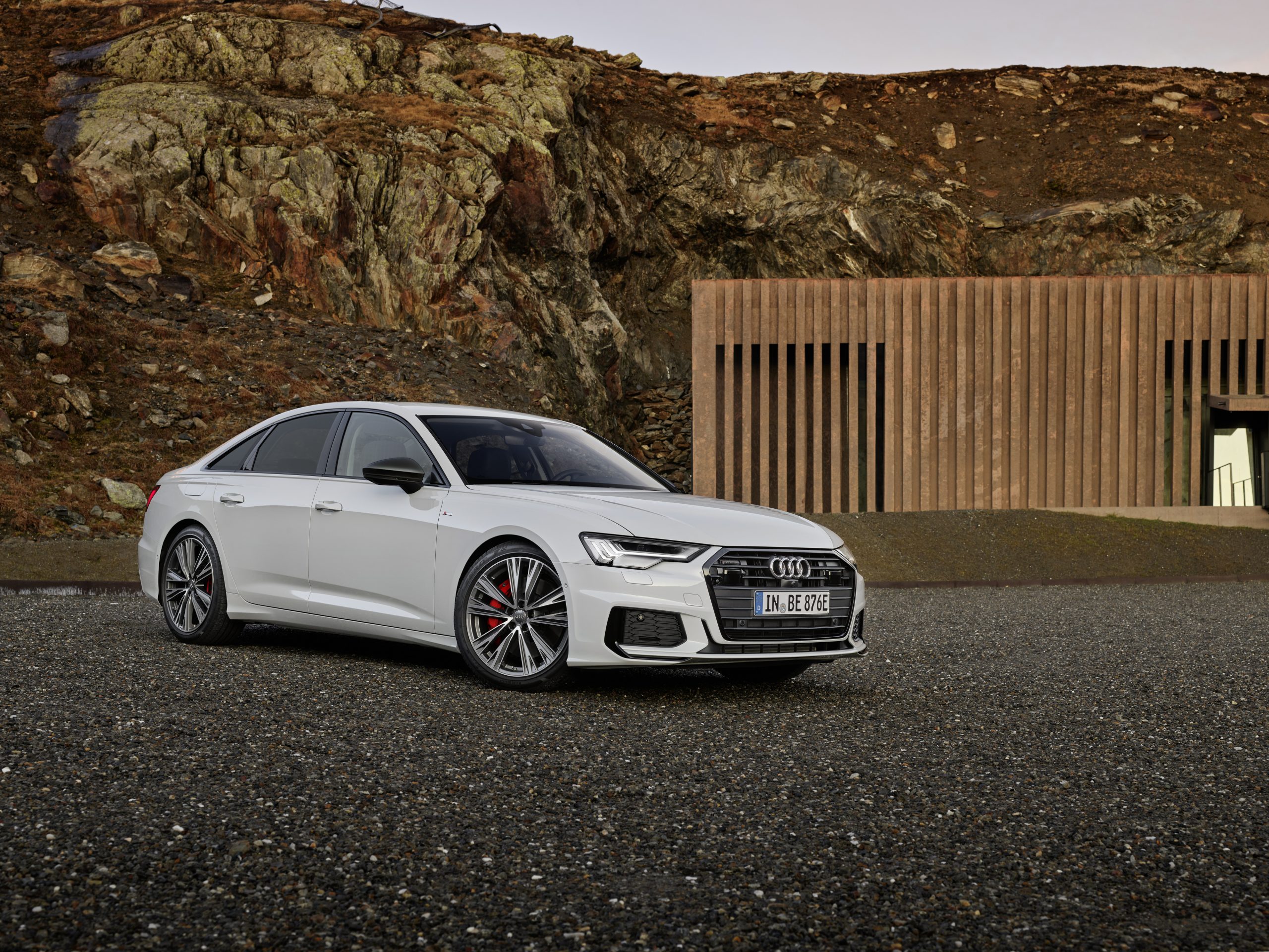A 3/4 front view of a white 2022 Audi A6 sedan parked on gravel with rocky cliffs in the background.