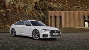 A 3/4 front view of a white 2022 Audi A6 sedan parked on gravel with rocky cliffs in the background.