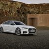 A 3/4 front view of a white 2022 Audi A6 sedan parked on gravel with rocky cliffs in the background.