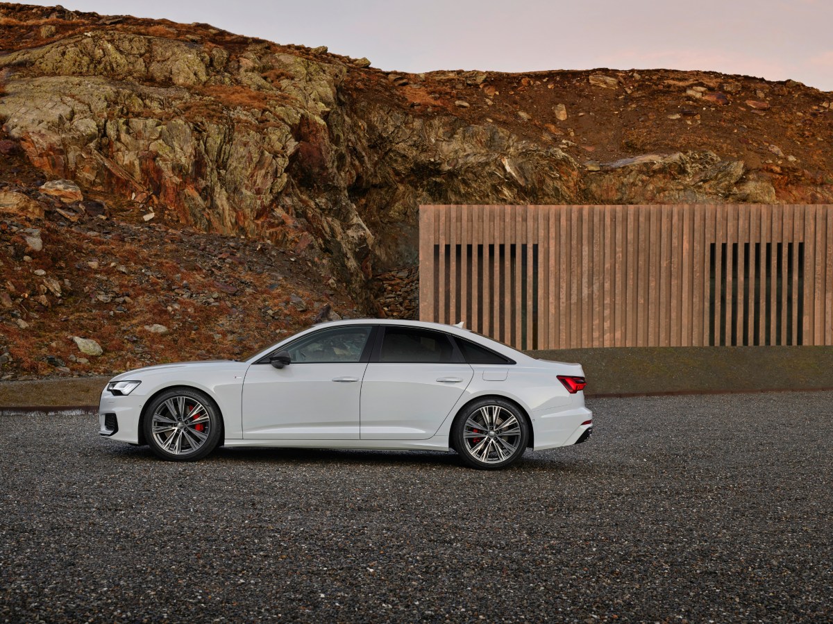 A profile view of a white 2022 Audi A6 sedan parked on gravel with rocky cliffs in the background