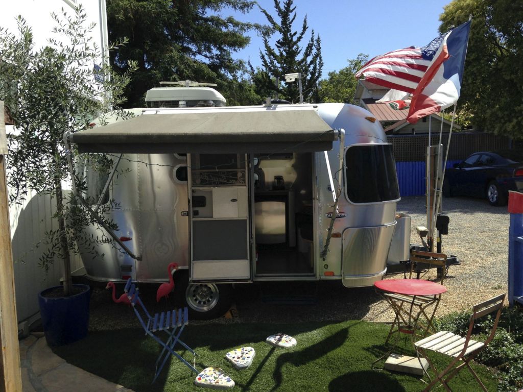 An Airstream Bambi parked outdoors with a rock path, American flag, and small table and chair.