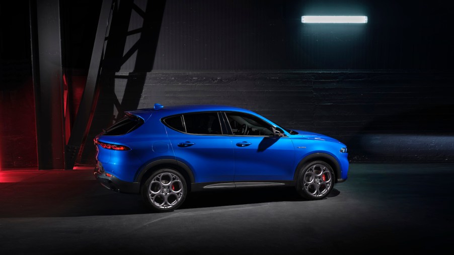 Promo shot of a blue Alfa Romeo Tonale or Dodge Hornet crossover SUV in front of a gray brick wall.