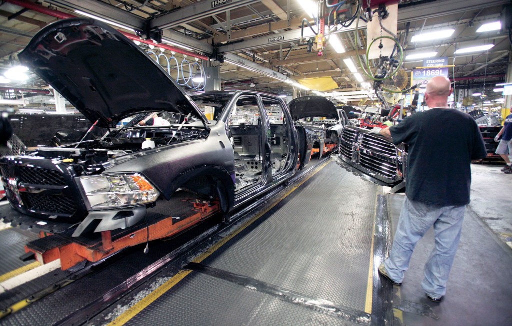 This is a Ram 1500 pickup truck with no doors or wheels being assembled by an autoworker in a factory.