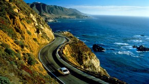 A white car drives near cliffs in Big Sur along California's Pacific coast