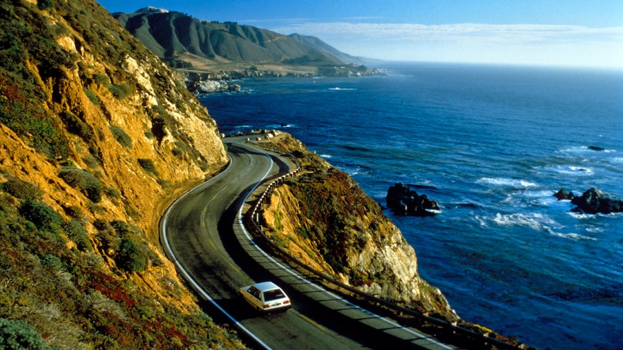 A white car drives near cliffs in Big Sur along California's Pacific coast