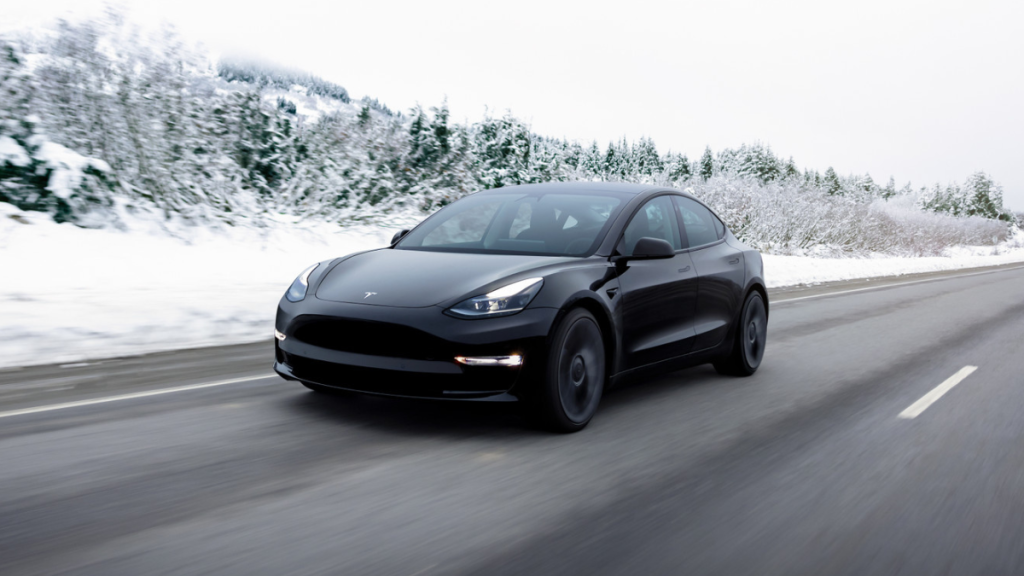 Black 2022 Tesla Model 3, the electric car with highest Consumer Reports owner satisfaction, driving by a snowy forest