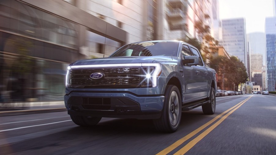 Blue 2022 Ford F-150 Lightning driving on a street, highlighting advantages of EVs vs. gas-powered cars
