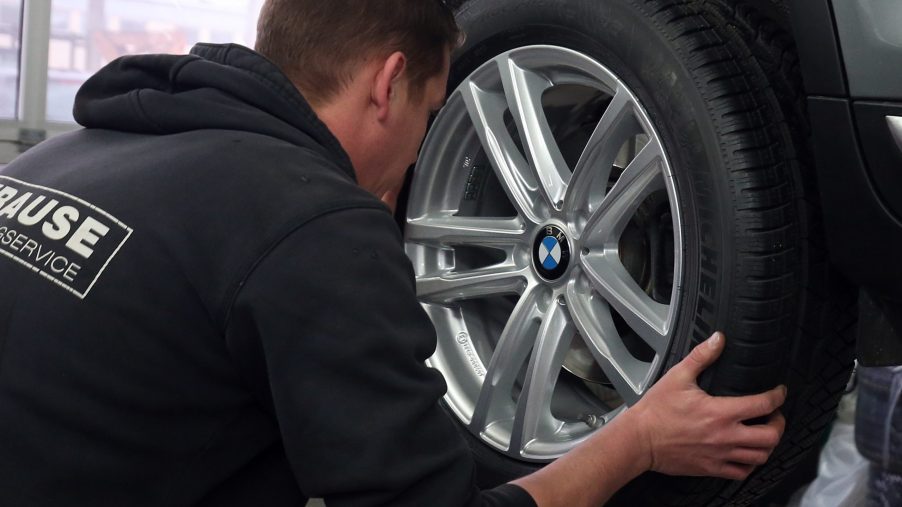 A man removes a car's wheel to inspect its wheel bearing