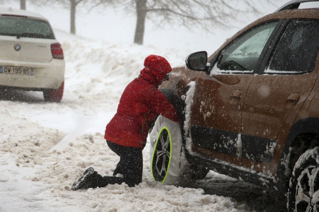 A woman lowering tire pressure and applying snow chains to her car in a snow strom