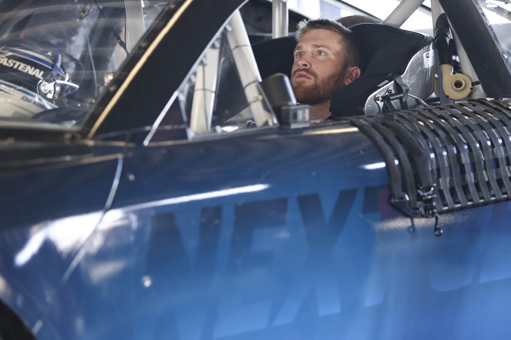 Driver Chris Buescher sits in a NASCAR car staring up at the rearview mirror or rearview camera screen.