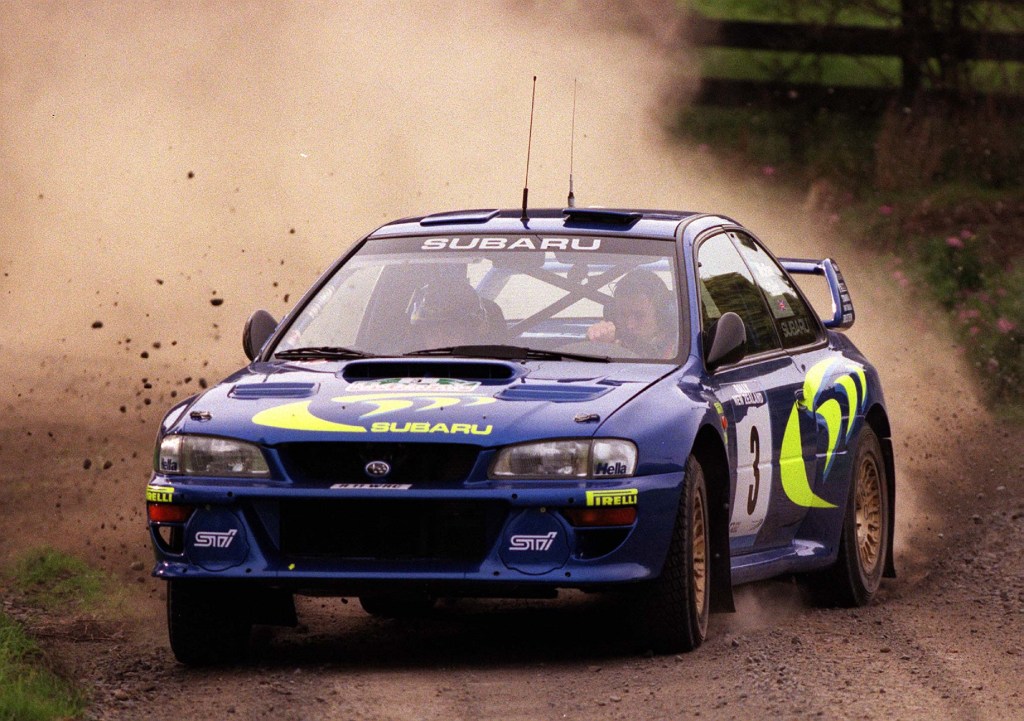 Colin McRae drifts his blue-and-yellow 1998 Subaru Impreza WRC rally car on a dirt rally stage