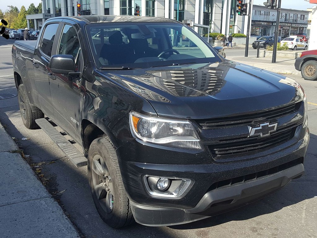 A Chevy Colorado sits on the side of the street, featuring running boards and a black paint job.