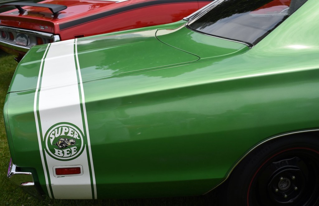 Rear quarter of a green muscle car at a car show with a prominent "Super Bee" decal inside a racing stripe.