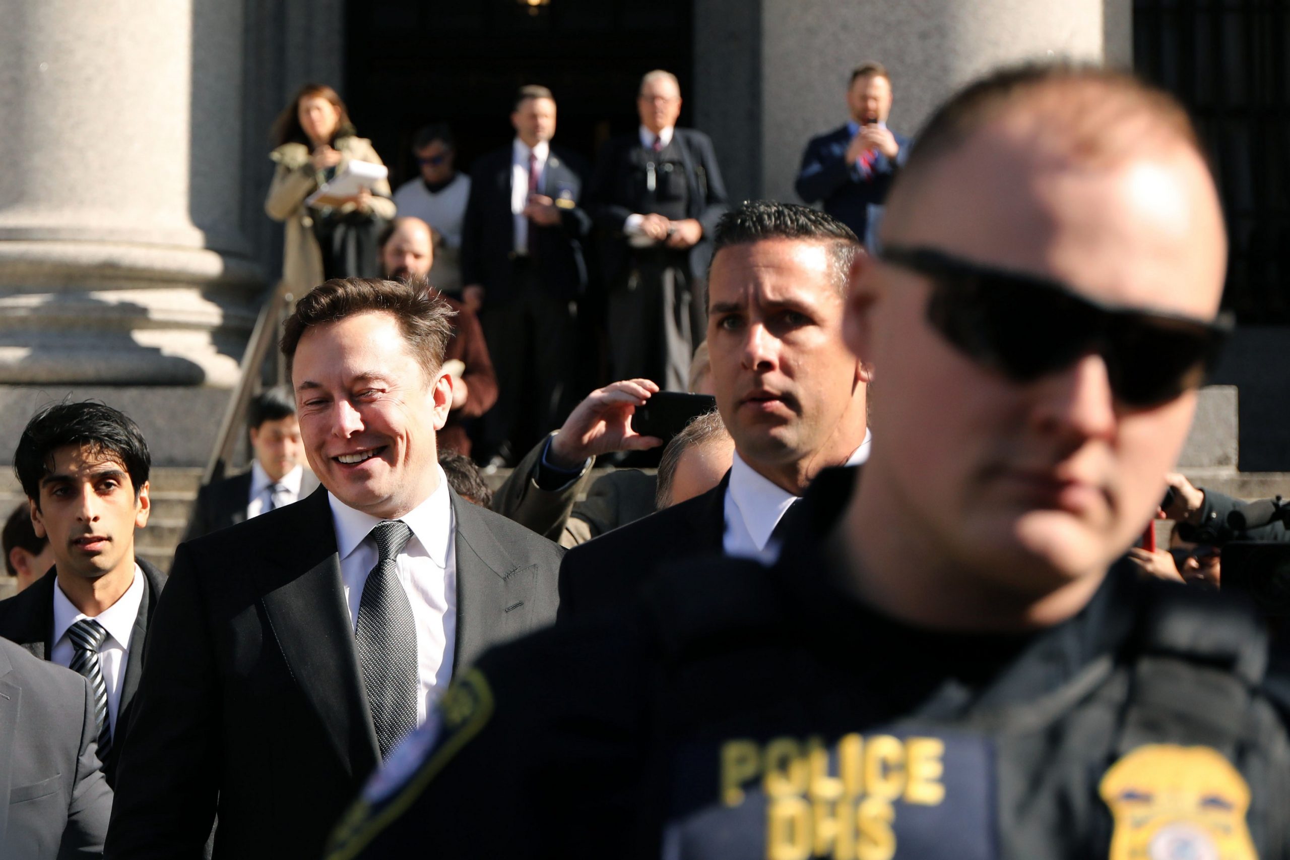 Elon Musk leaving a federal court hearing surrounded by police and security